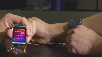 A stretchable battery has been sewn inside an elastic strap worn on the arm, at right. The battery can power a smart watch.