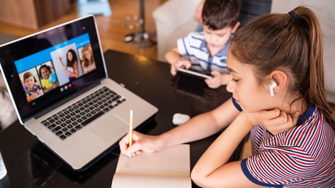 a girl on a computer attending a virtual lesson and a boy at the same table on his tablet
