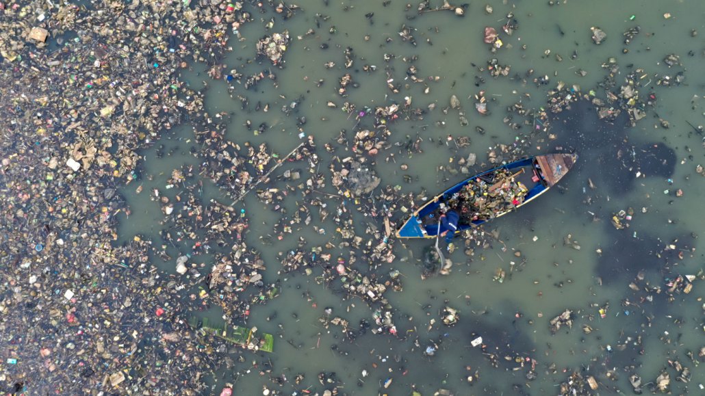 a canoe floats through water cluttered with plastic trash