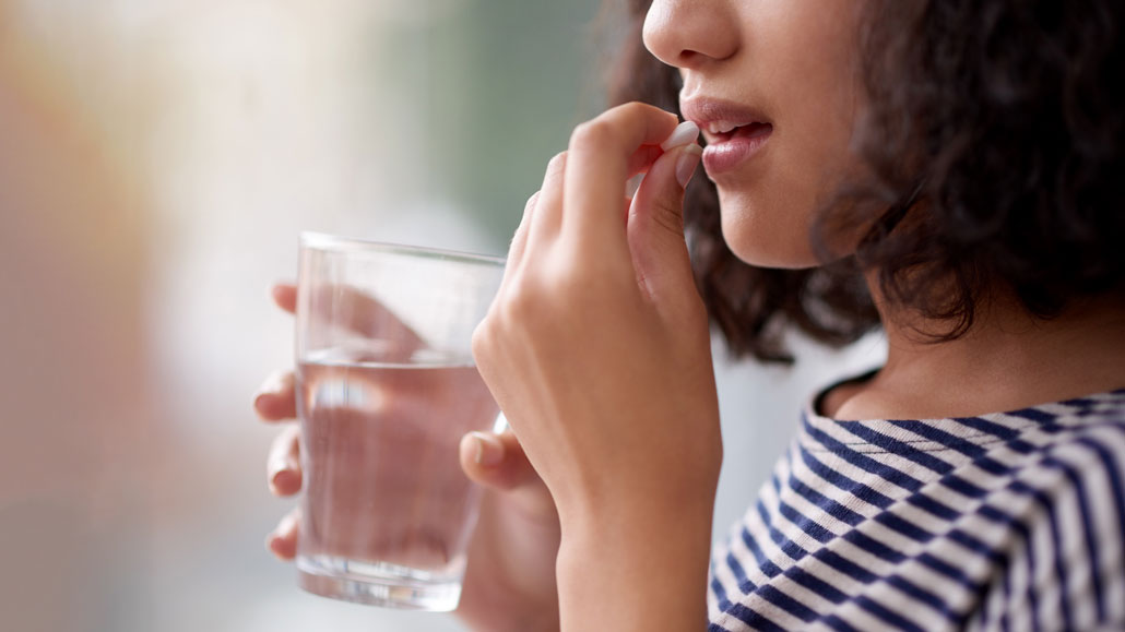 a close up of a woman holding a glass of water and putting a pill in her mouth