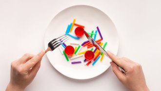 an image of hands holding a fork and knife over a white plate full of bottle caps and cut up drinking straws
