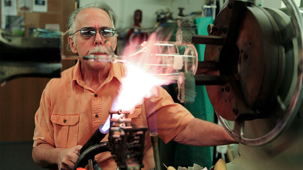 a photo of an older white man concentrating shaping a specialized flask with fire