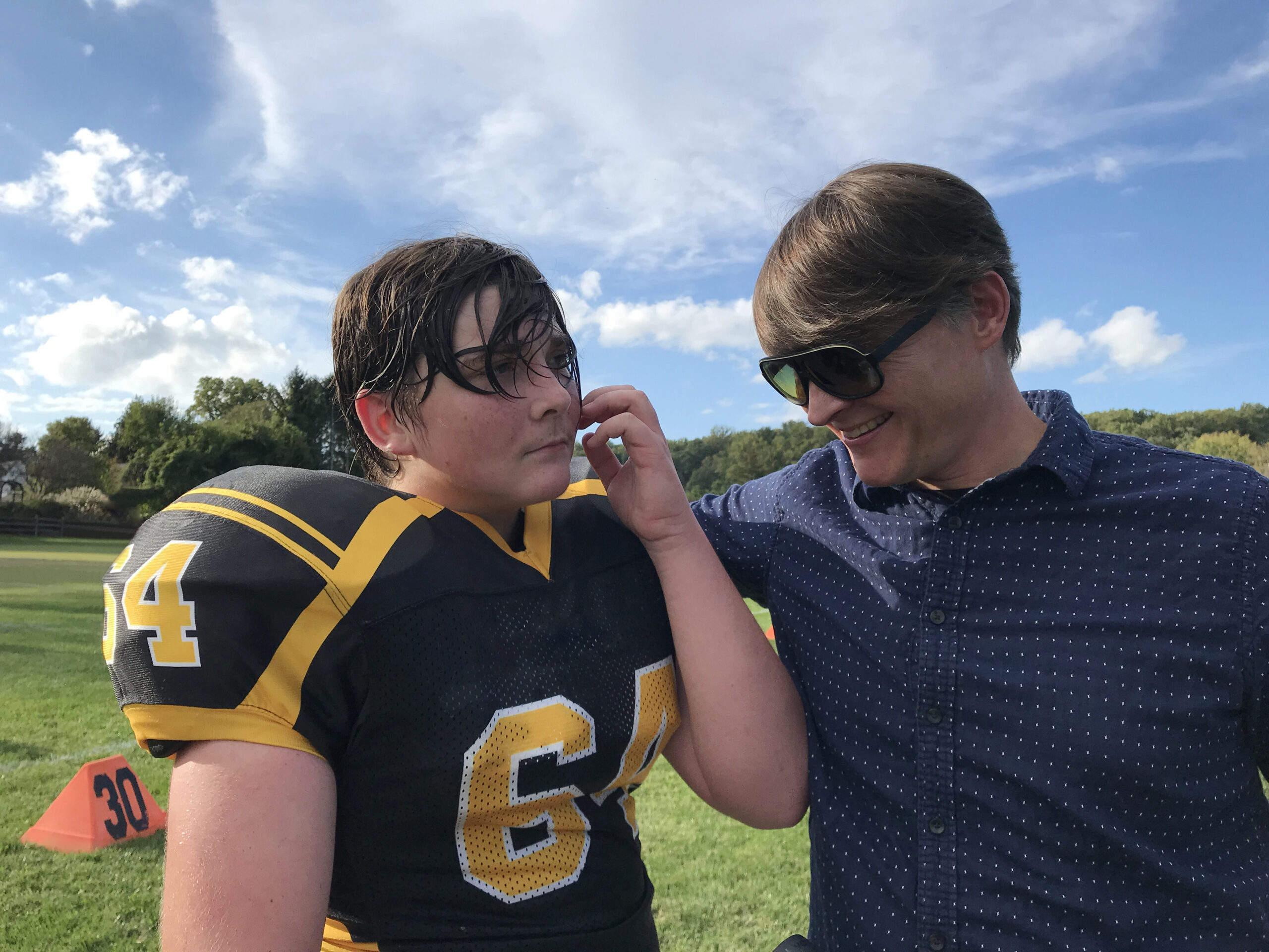 A father wraps an arm around his son, a sweaty teen boy in a football uniform