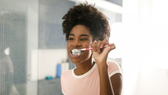 a Black teen with braces brushes her teeth