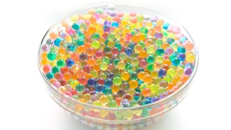 a glass bowl is filled to the brim with shiny wet orbs of all different colors