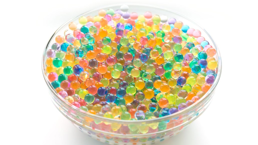 a glass bowl is filled to the brim with shiny wet orbs of all different colors