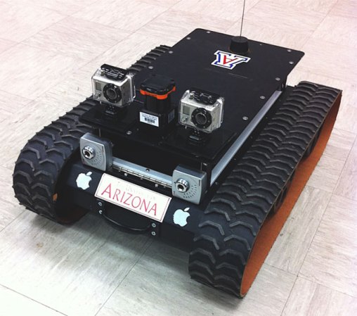 a photo of a small rectangular rover. It has treads on the long side of the rectangle. On the short side of the rectangle, facing the viewer, two cameras are mounted looking forward, they alost look like eyes. 