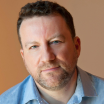 Author Adrian Dingle sits in front of an orange background.