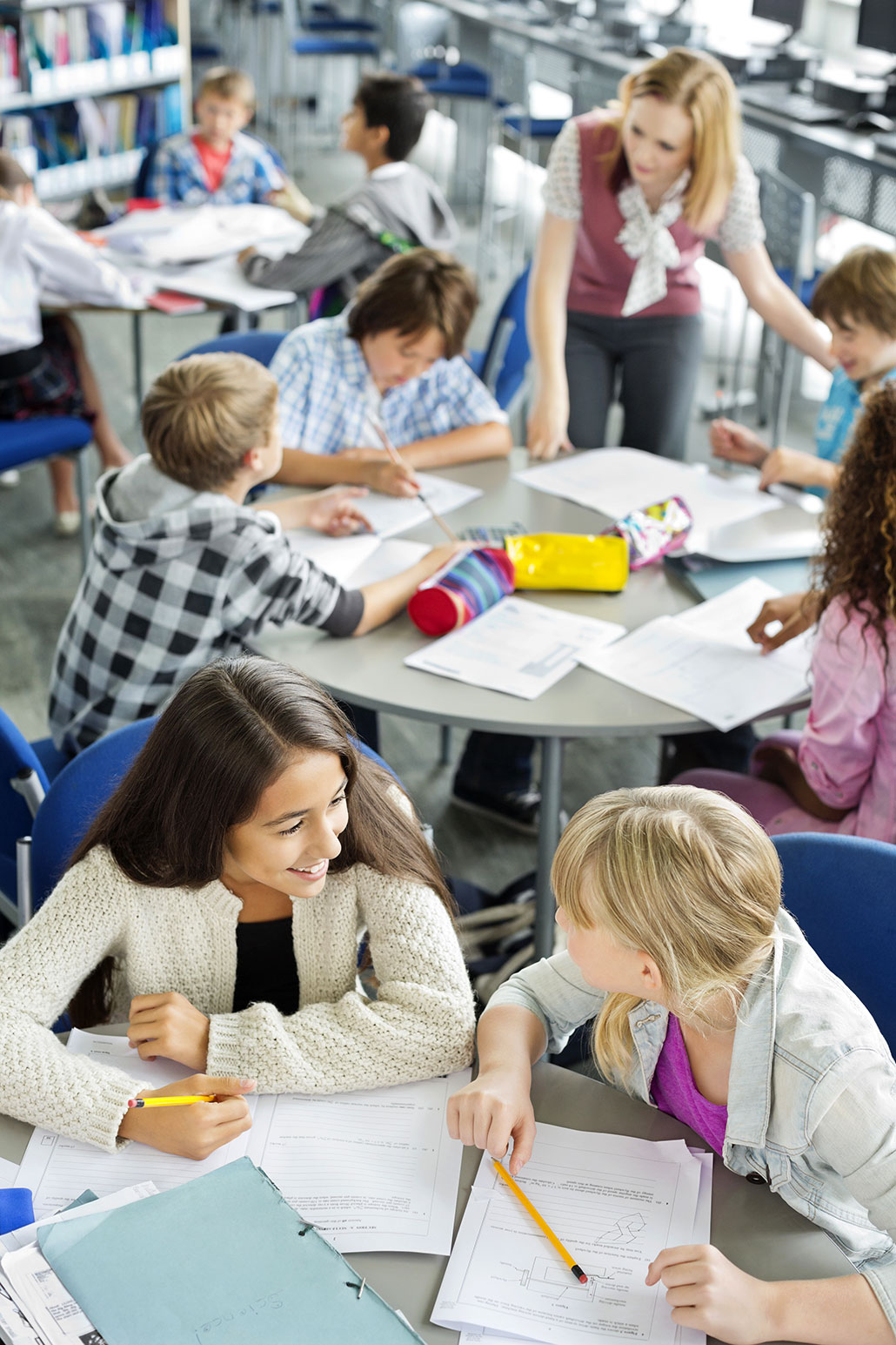 a group of kids doing classwork and sitting closely together at several round tables