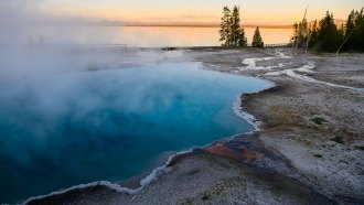 a clear pool of water with crystals at the edges is steaming as the sun sets