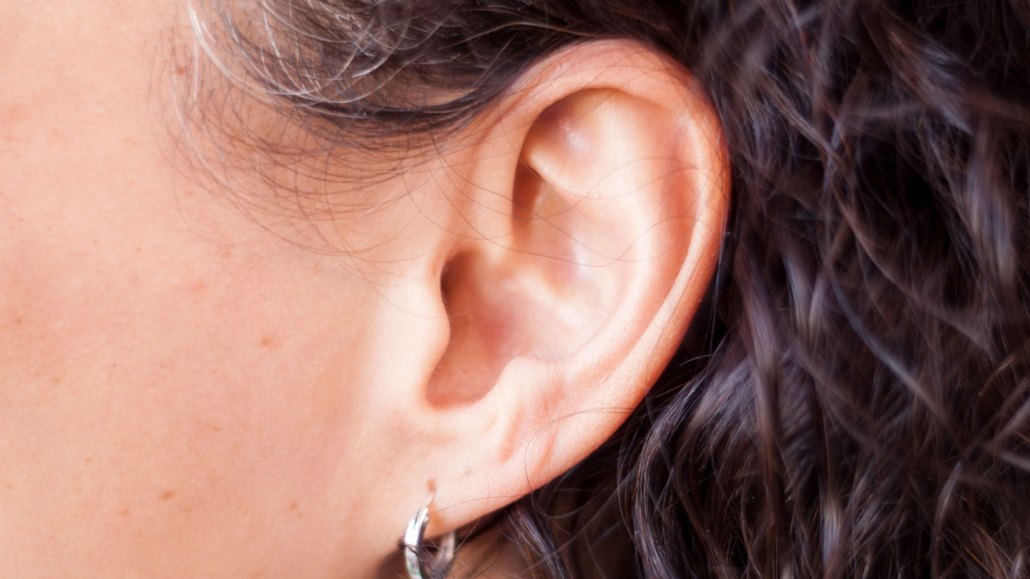 A close-up photograph shows an ear with a silver hoop earring and black wavy hair behind the ear.