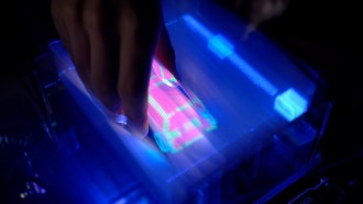 a hand reaches down into an illuminated screen displaying a virtual 3-D graphic of a car