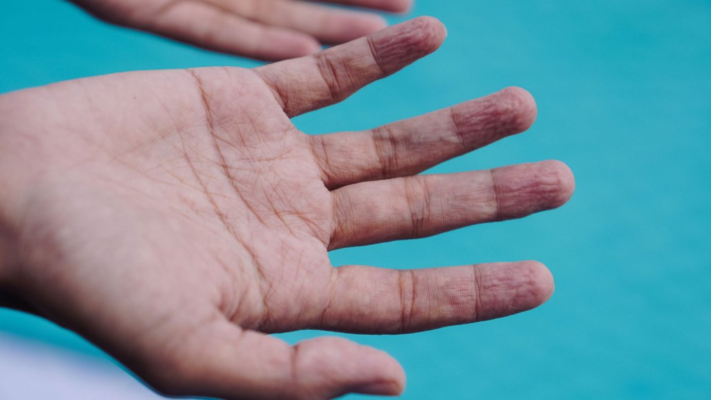 A hand with wrinkly fingertips held above a swimming pool.