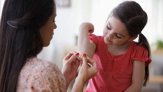 an adult opening a bandaid to put on a girl's elbow
