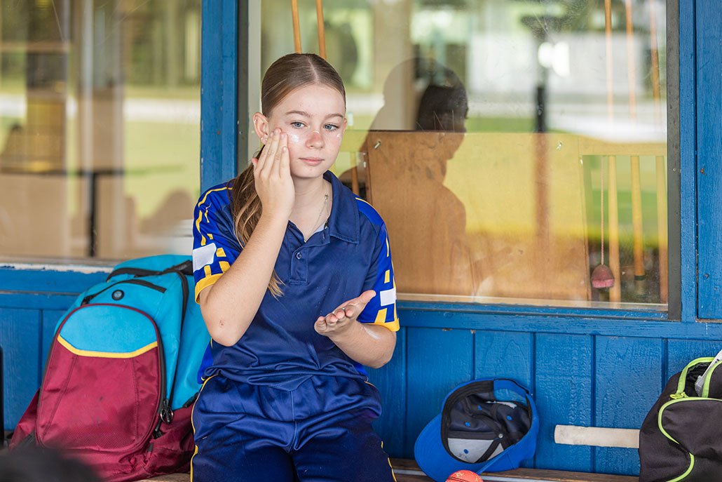 a girl dressed in athletic clothing sits under shade and applies sunscreen to her face