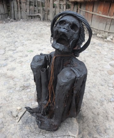 The image shows a modern-day mummified person with their jaws open and their body folded so the knees touch the shoulders.
