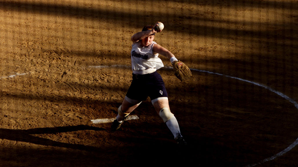 A woman winds up to throw a softball on a playing field