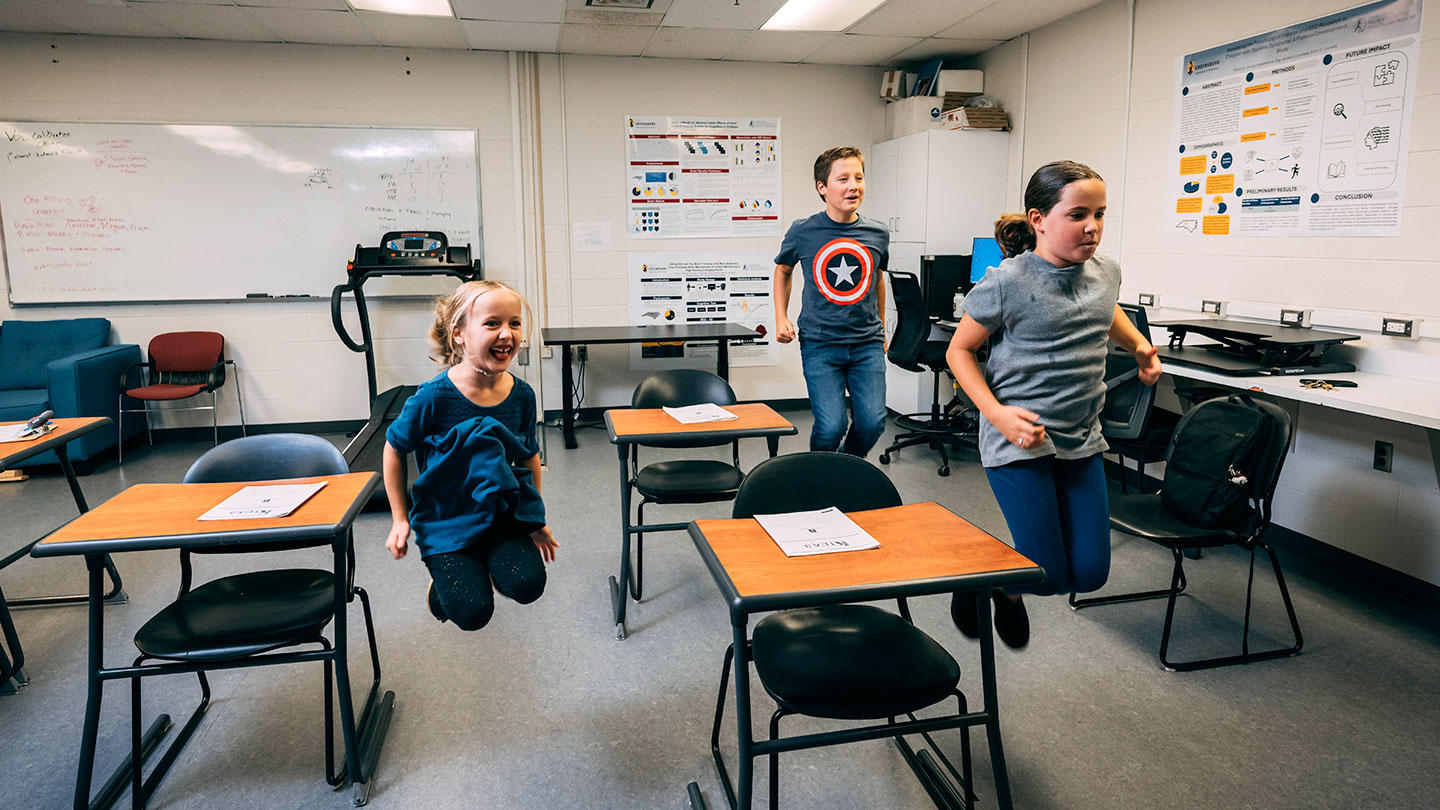 three students in a classroom jumping at their desks