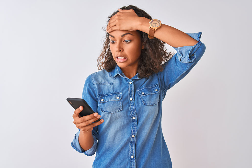 a woman looks at her phone with dismay and puts her other hand on her head
