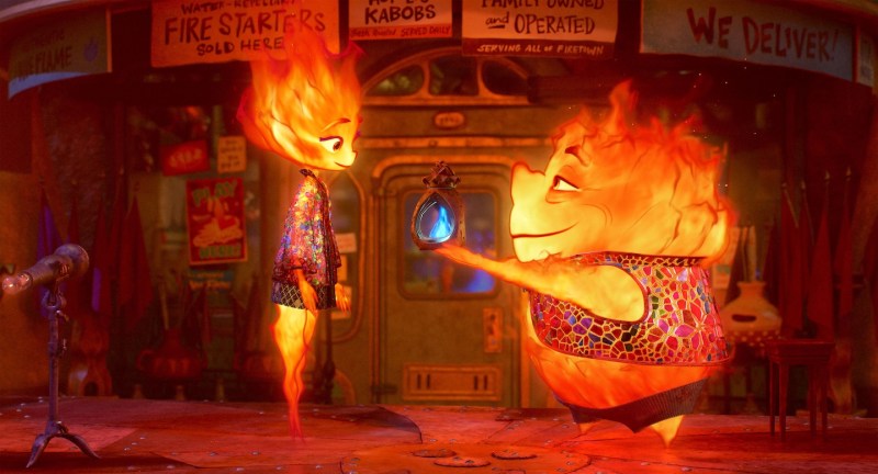 two people made of fire face each other, one young woman and one shorter, older man handing her a bright blue flame
