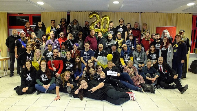 a large group of people posted for a picture, with balloons spelling "20" in the background